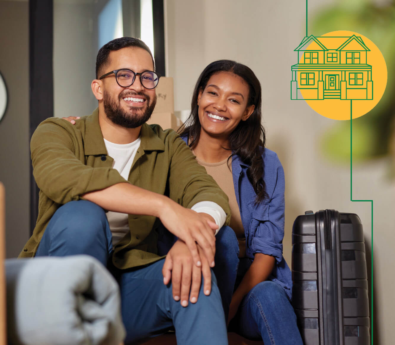 A couple sitting down next to a suitcase surrounded by moving furniture.